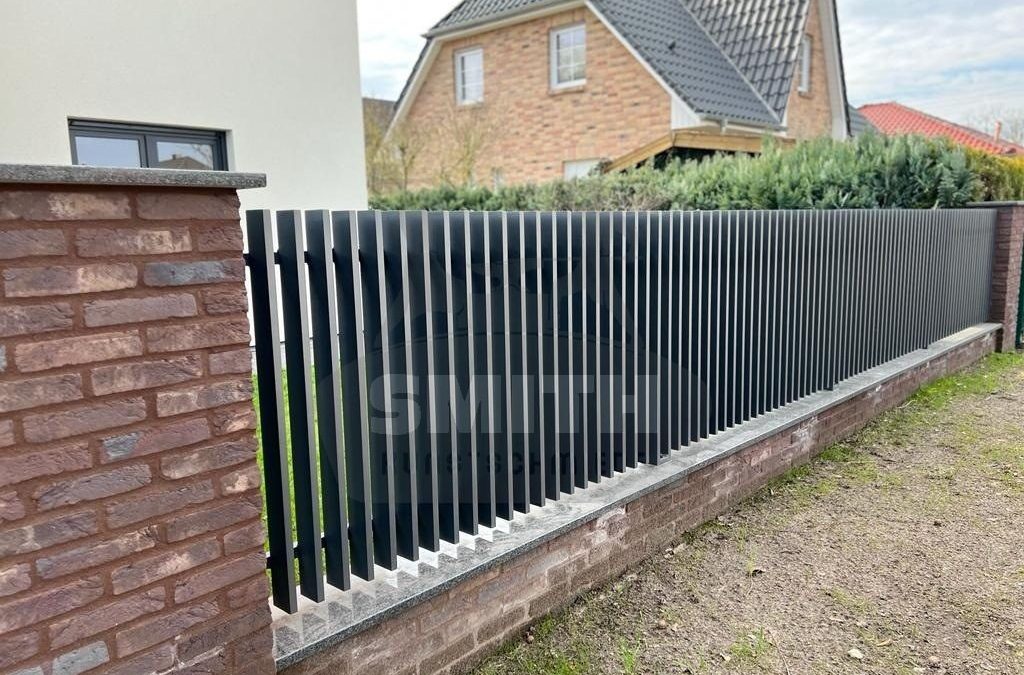Metallzaun aus senkrechten Stäben auf einer Klinkermauer an der Grundstücksgrenze